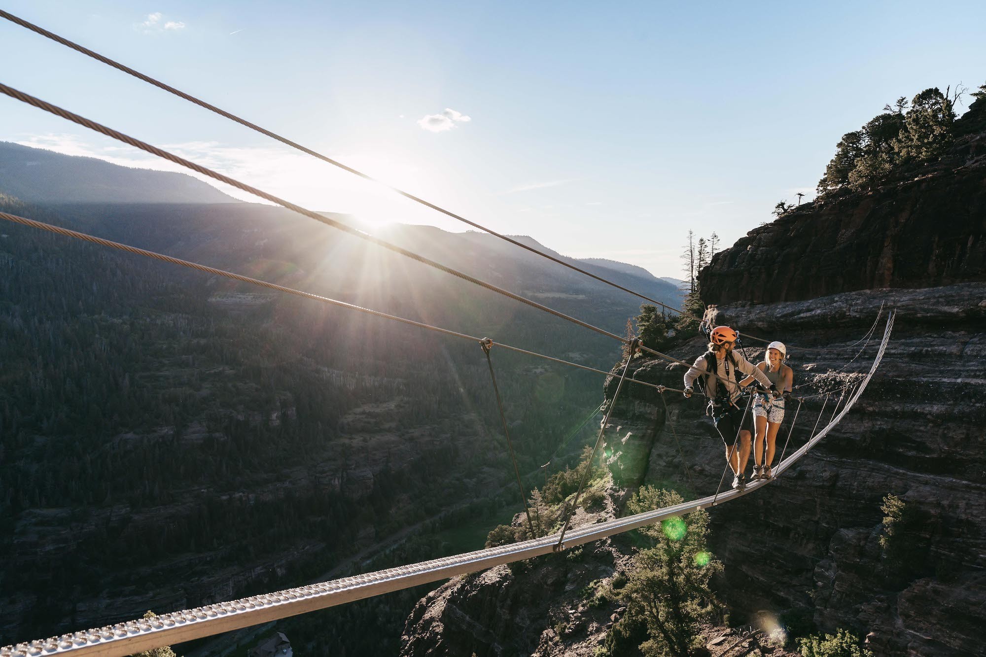 Zwei Menschen überqueren gesichert eine schmale Hängebrücke hoch über einer Schlucht in Ouray, Colorado