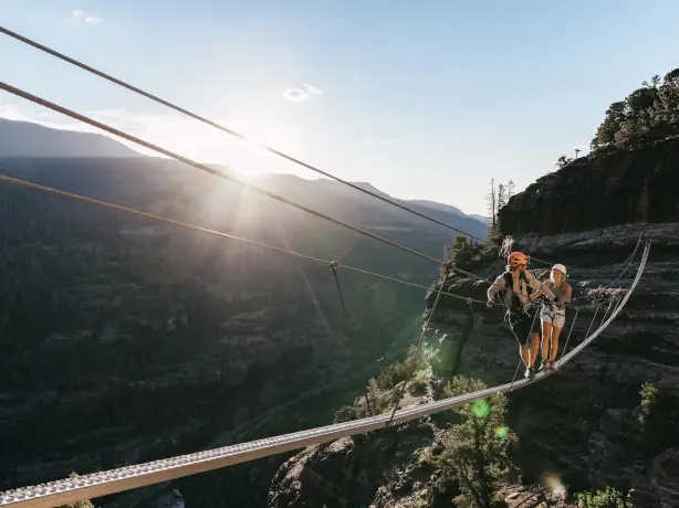 Zwei Menschen überqueren gesichert eine schmale Hängebrücke hoch über einer Schlucht in Ouray, Colorado