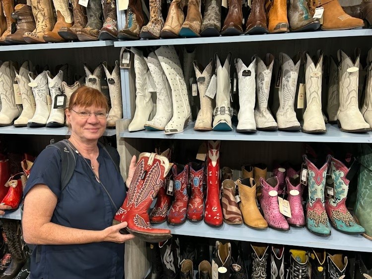 Frau steht vor Regal mit Cowboystiefeln und hält einen roten Stiefel in der Hand