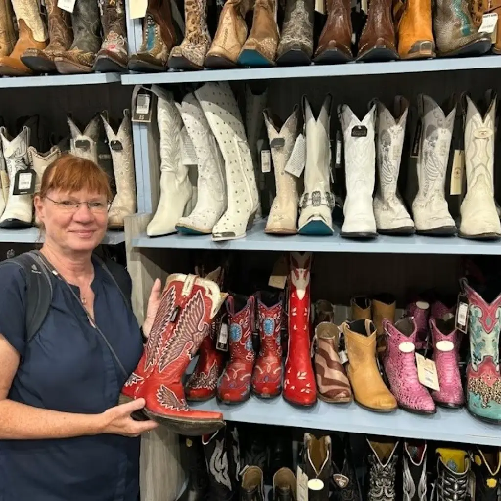 Frau steht vor Regal mit Cowboystiefeln und hält einen roten Stiefel in der Hand