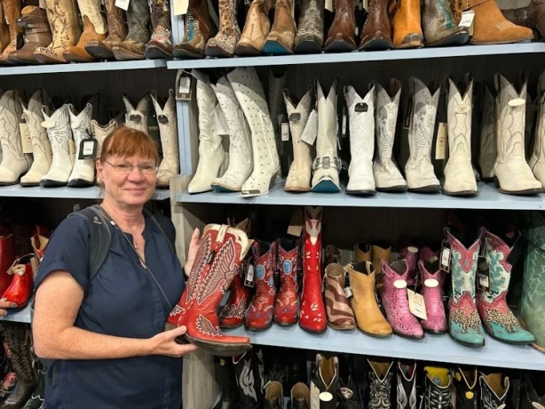 Frau steht vor Regal mit Cowboystiefeln und hält einen roten Stiefel in der Hand