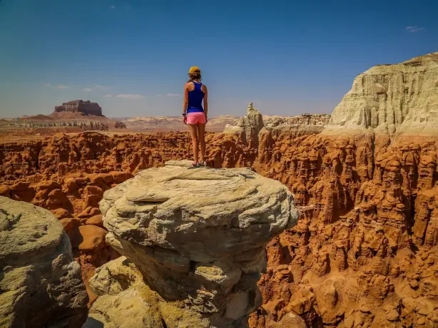 Ein Wanderer steht auf einem Felsvorsprung und überblickt die geformten roten Felsformationen und die Wüstenlandschaft des amerikanischen Südwestens.