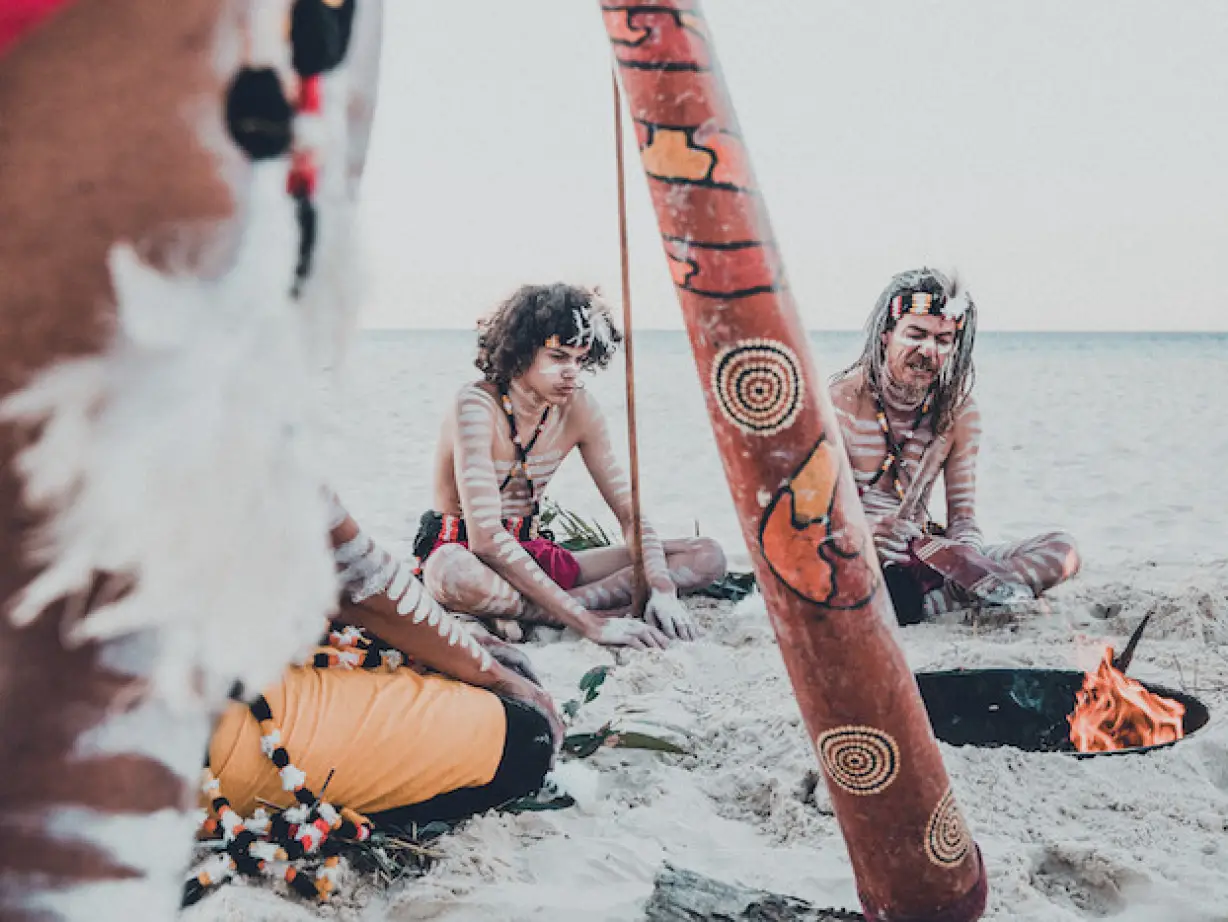 Eine Gruppe von Menschen mit Körperbemalung sitzt um ein Feuer herum Redland Küste, Australien