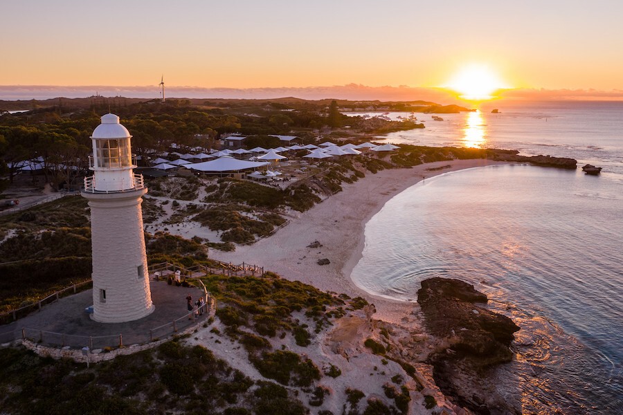 A lighthouse on the coast with a sunset in the background