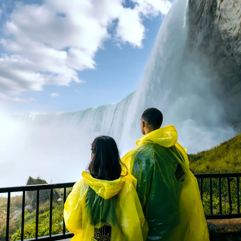 A couple wearing waterproof ponchos look up at the thundering Niagara Falls in Canada
