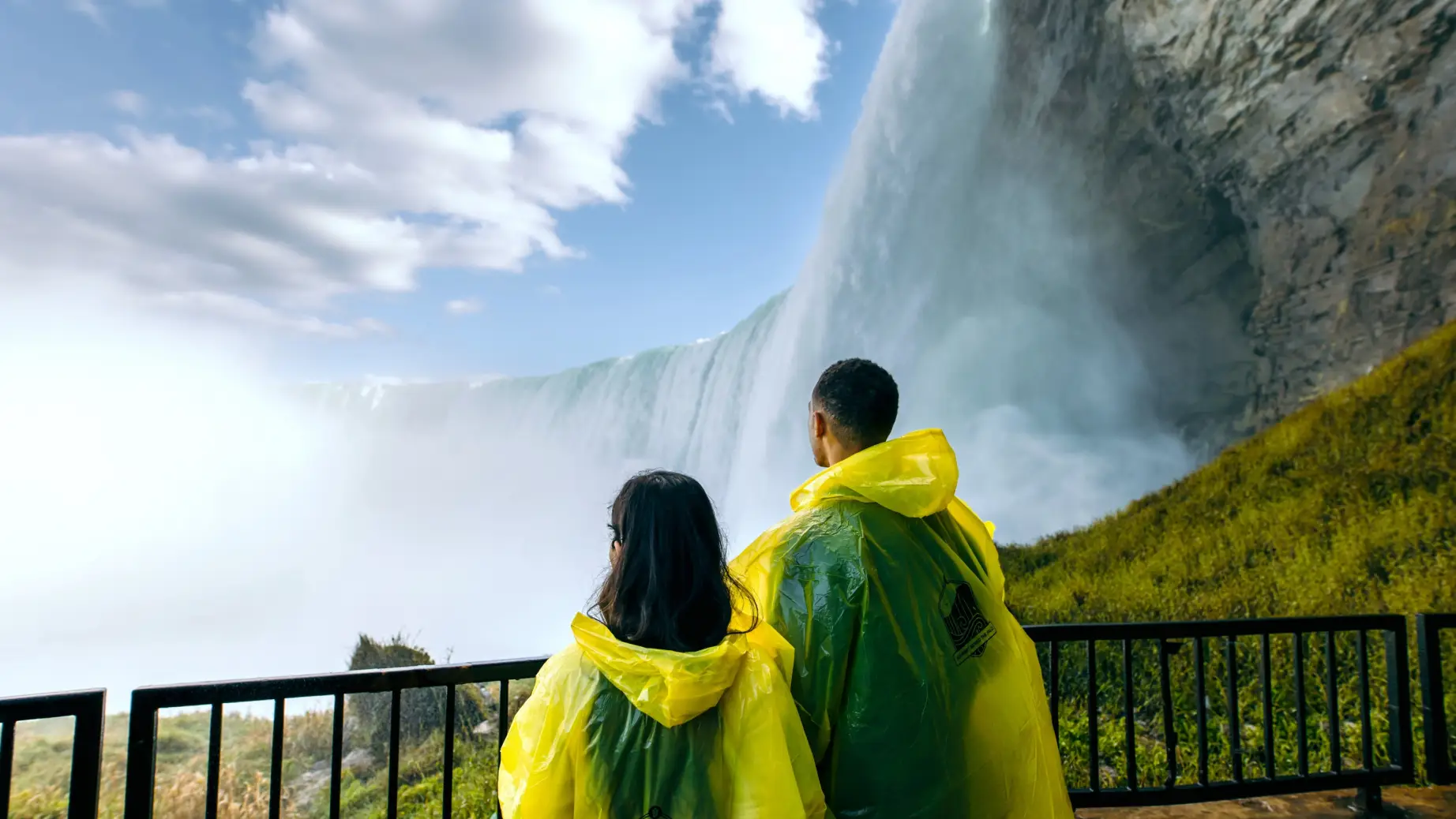 A couple wearing waterproof ponchos look up at the thundering Niagara Falls in Canada